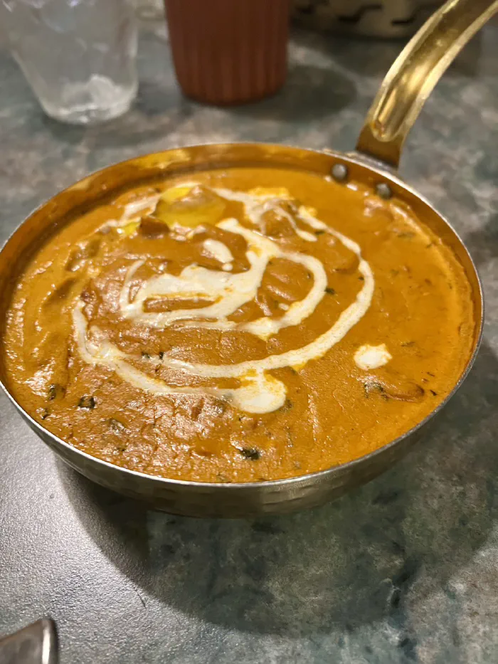 真鍮の小鍋に盛られた、生クリームがかかった濃厚なカレー